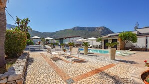 A pool area with lounge chairs and umbrellas, surrounded by stone tiles and potted plants. - Nice home in Terrasini (Terrasini)