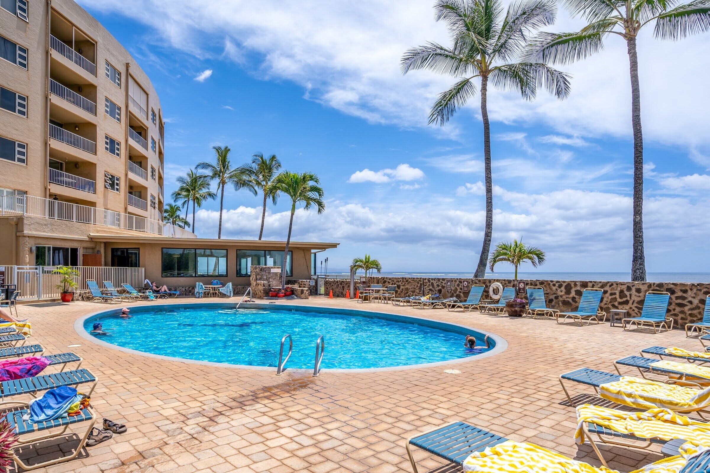 A pool area with lounge chairs, palm trees, and a building with balconies.