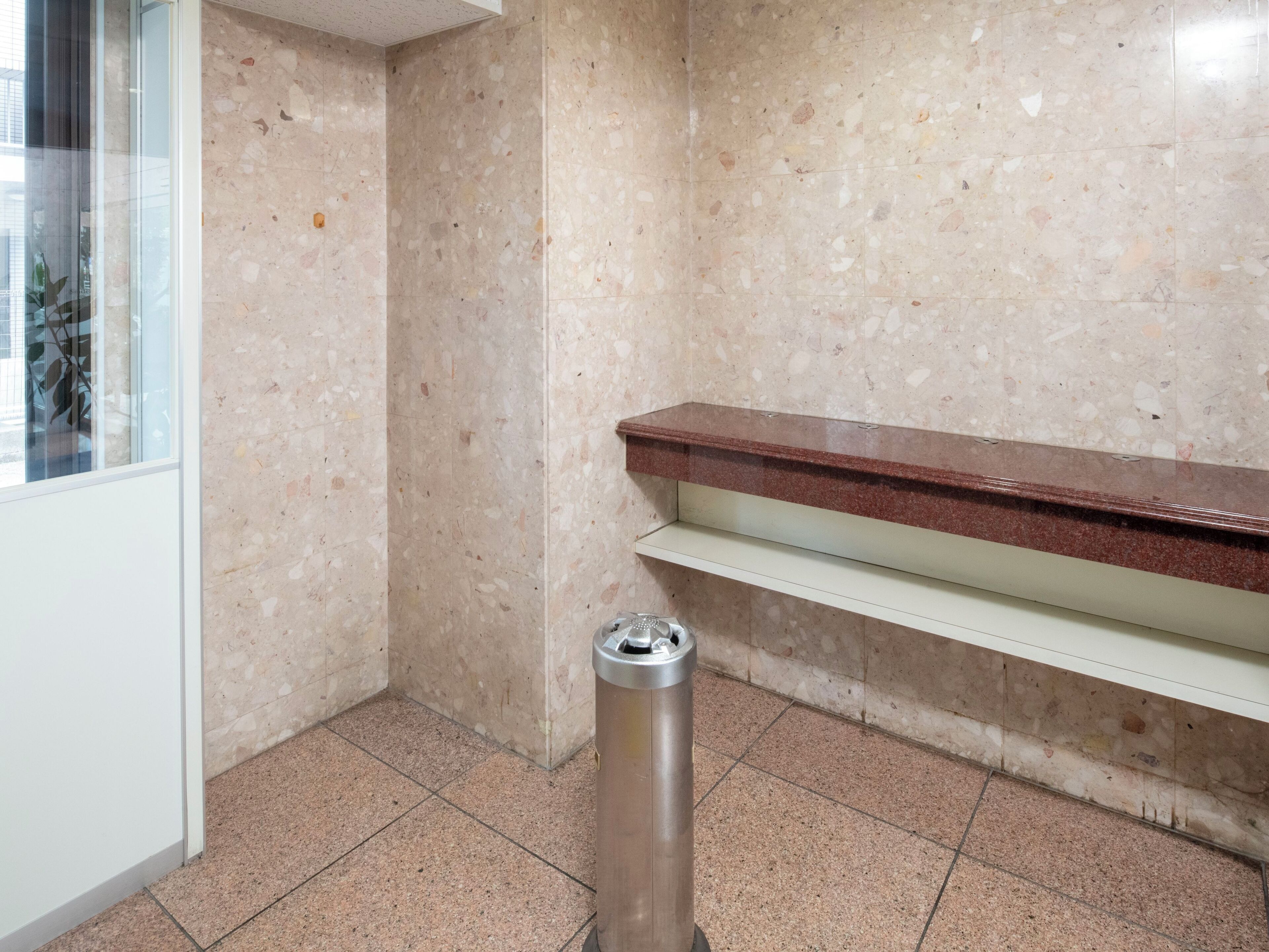 A corner of a room with a marble wall, a metal trash bin, and a wooden counter.