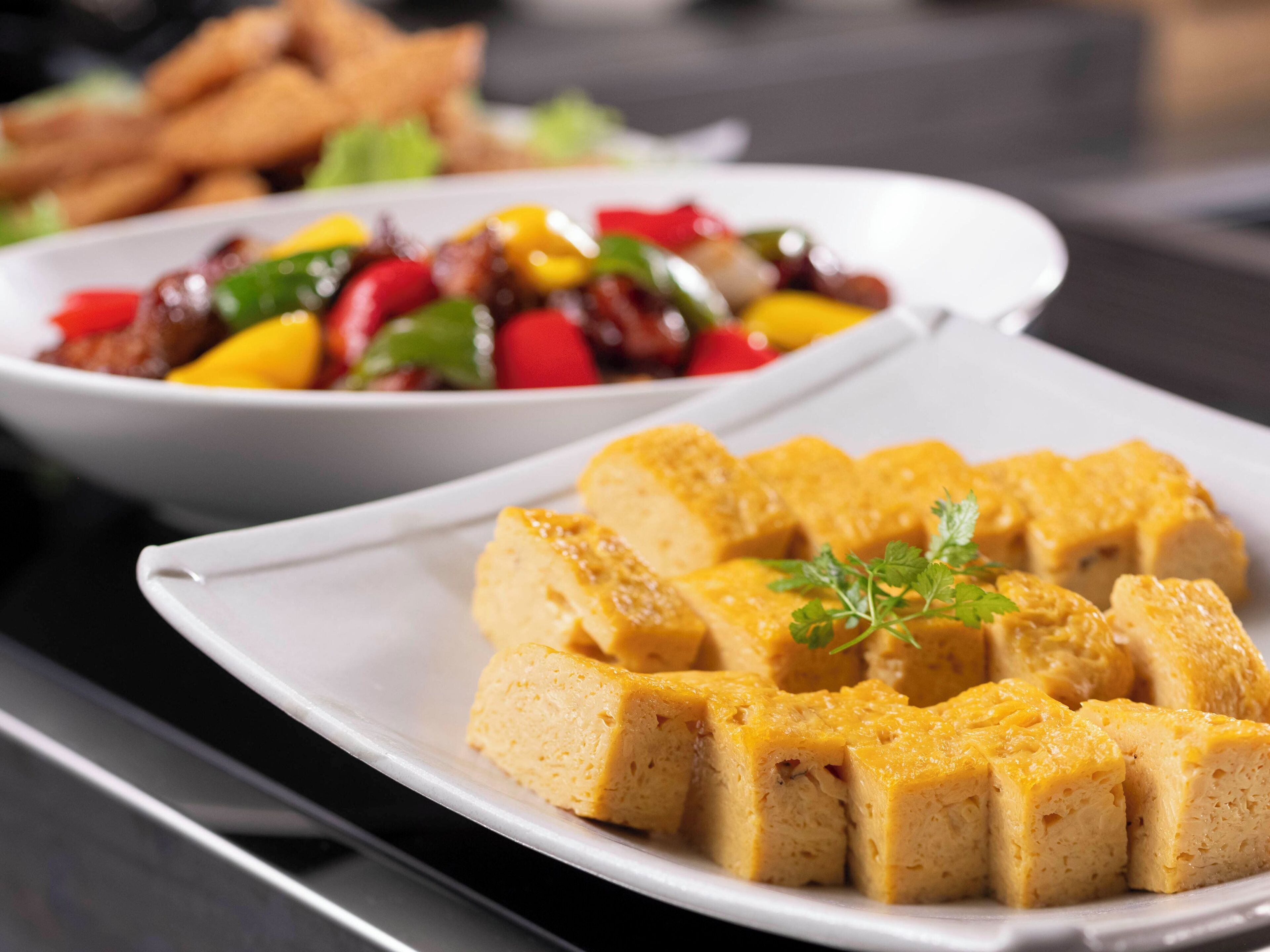 Une assiette de cubes de tofu garnis de persil, un bol de légumes variés et, au fond, une assiette de plats frits.