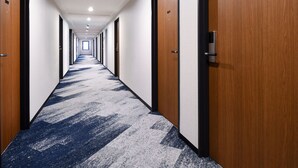 A hotel hallway with a carpeted floor, wooden doors, and a number "310" on one door. - HOTEL MYSTAYS Atsugi (Atsugi)