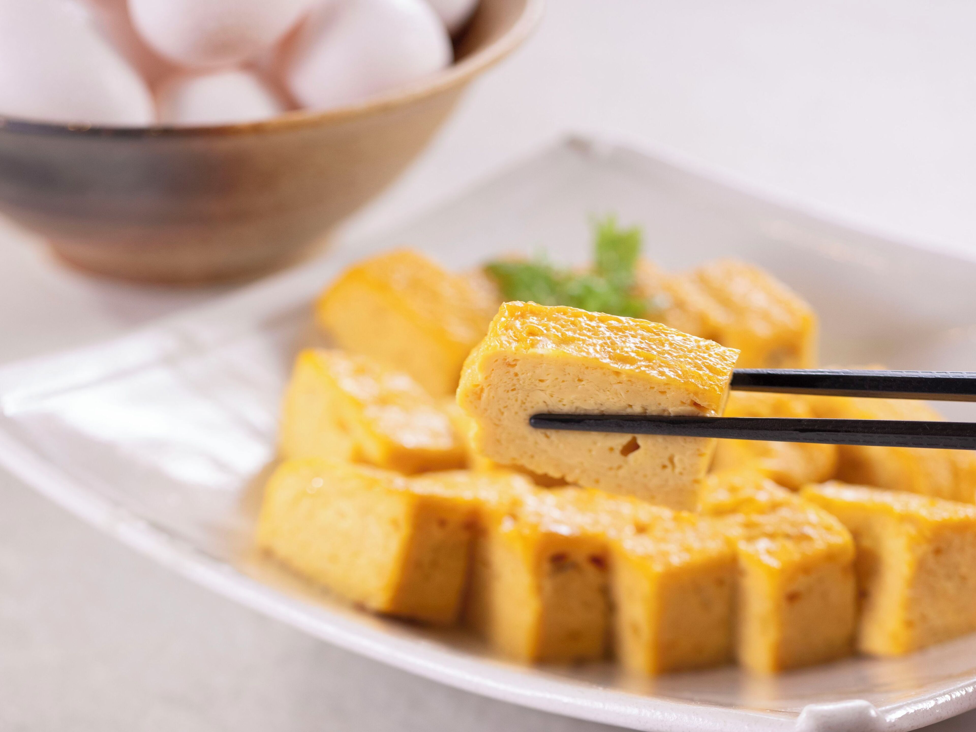 Een bord met blokjes tofu, stokjes pakken er een.