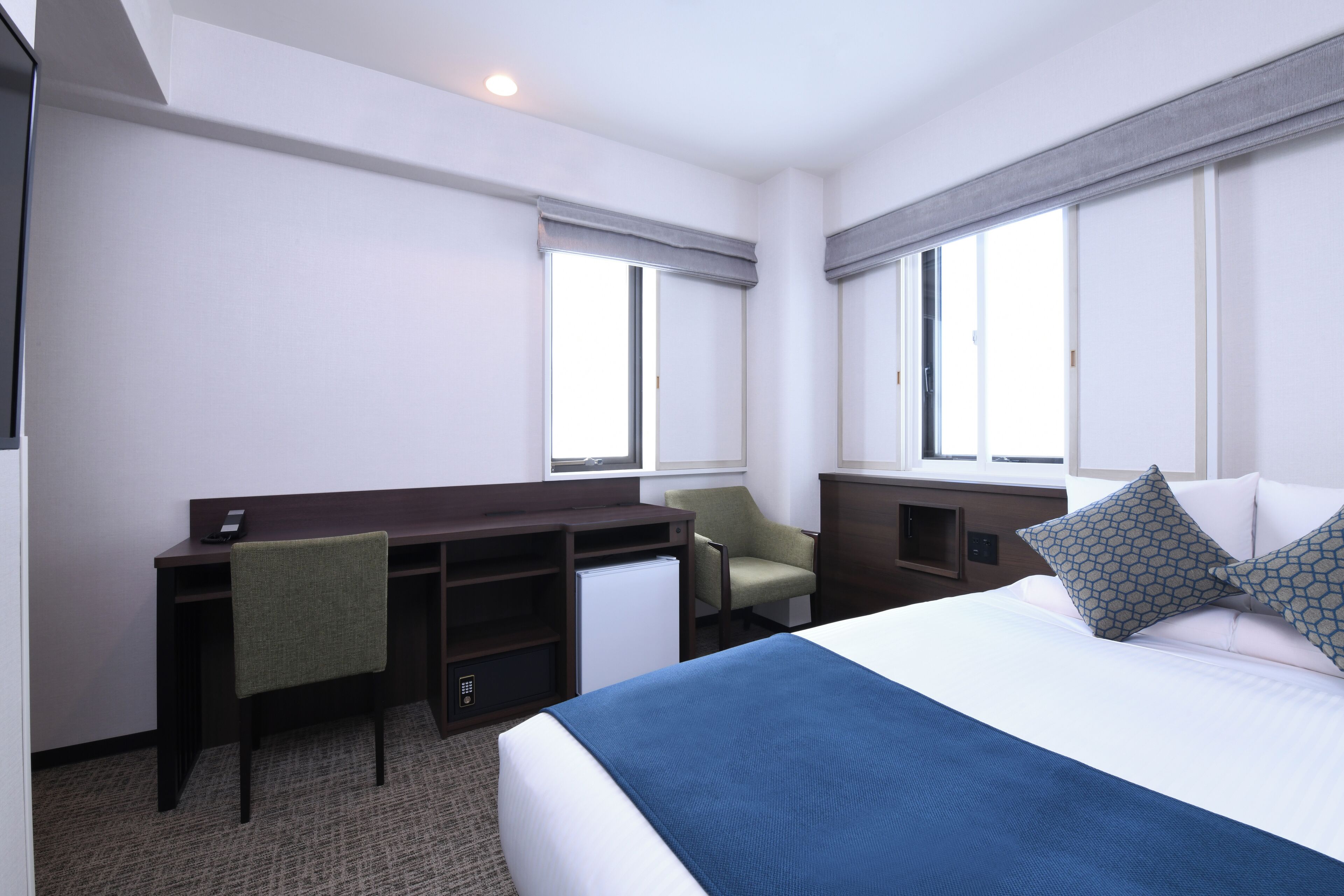 A hotel room with a bed, a desk, a chair, and a small refrigerator.