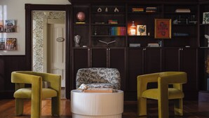 A living room with a round white ottoman, two green chairs, a patterned armchair, and a bookshelf filled with books and decorative items. - Harpswell Inn (Harpswell)