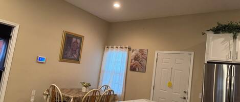 A dining area with a table and chairs, a painting on the wall, a thermostat, and a refrigerator.