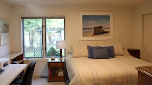 Un dormitorio con cama, escritorio, silla, mesita de noche, ventana y un cuadro de un barco en la playa.