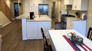 Una cocina moderna con armarios blancos, una isla central, una mesa de comedor con camino de mesa con bandera estadounidense y una escalera que lleva a otro nivel.