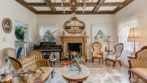 A spacious living room with a grand piano, elegant chairs, a chandelier, and a fireplace. - Banyan House Vacation Rentals (Venice)