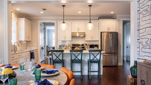 A modern kitchen with white cabinets, stainless steel appliances, and a dining area with a round table and orange chairs. - Luxury Design, Prime Location 2 Minutes from Midtown, Family Fun! (Memphis)