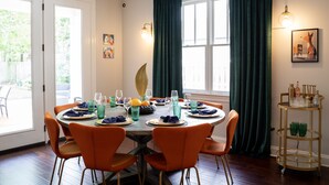 A dining area with a round table set for four, surrounded by orange chairs, with a window and curtains in the background. - Luxury Design, Prime Location 2 Minutes from Midtown, Family Fun! (Memphis)
