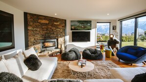 Una sala de estar moderna con chimenea de piedra, asientos cómodos, televisor de pantalla plana y vistas a las montañas.