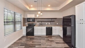 A modern kitchen with a central island, white cabinetry, a black refrigerator, and a hanging light fixture. - Charming 2-Bed Apartment in Houston (Houston)