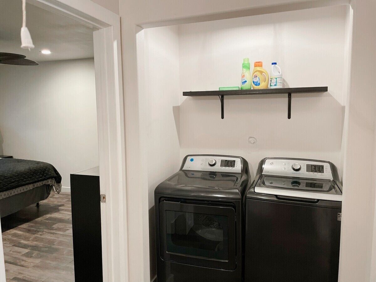 A laundry room with two washing machines and a shelf above them holding cleaning supplies.