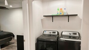 A laundry room with two washing machines and a shelf above them holding cleaning supplies. - Charming 2-Bed Apartment in Houston (Houston)