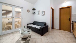 A modern living room with a black leather sofa, a glass coffee table, and a dining area with a table and chairs. There are framed pictures on the wall and a wooden door. - Holiday apartment with air conditioning and Internet (Zambratija)