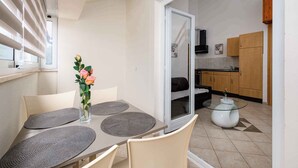 A dining area with a table, chairs, and a vase with flowers. There is a sliding glass door leading to a kitchen with wooden cabinets and a refrigerator. - Holiday apartment with air conditioning and Internet (Zambratija)