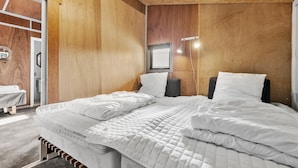 A bedroom with a wooden wall, a bed with white bedding, a bedside table, and a window with a view.