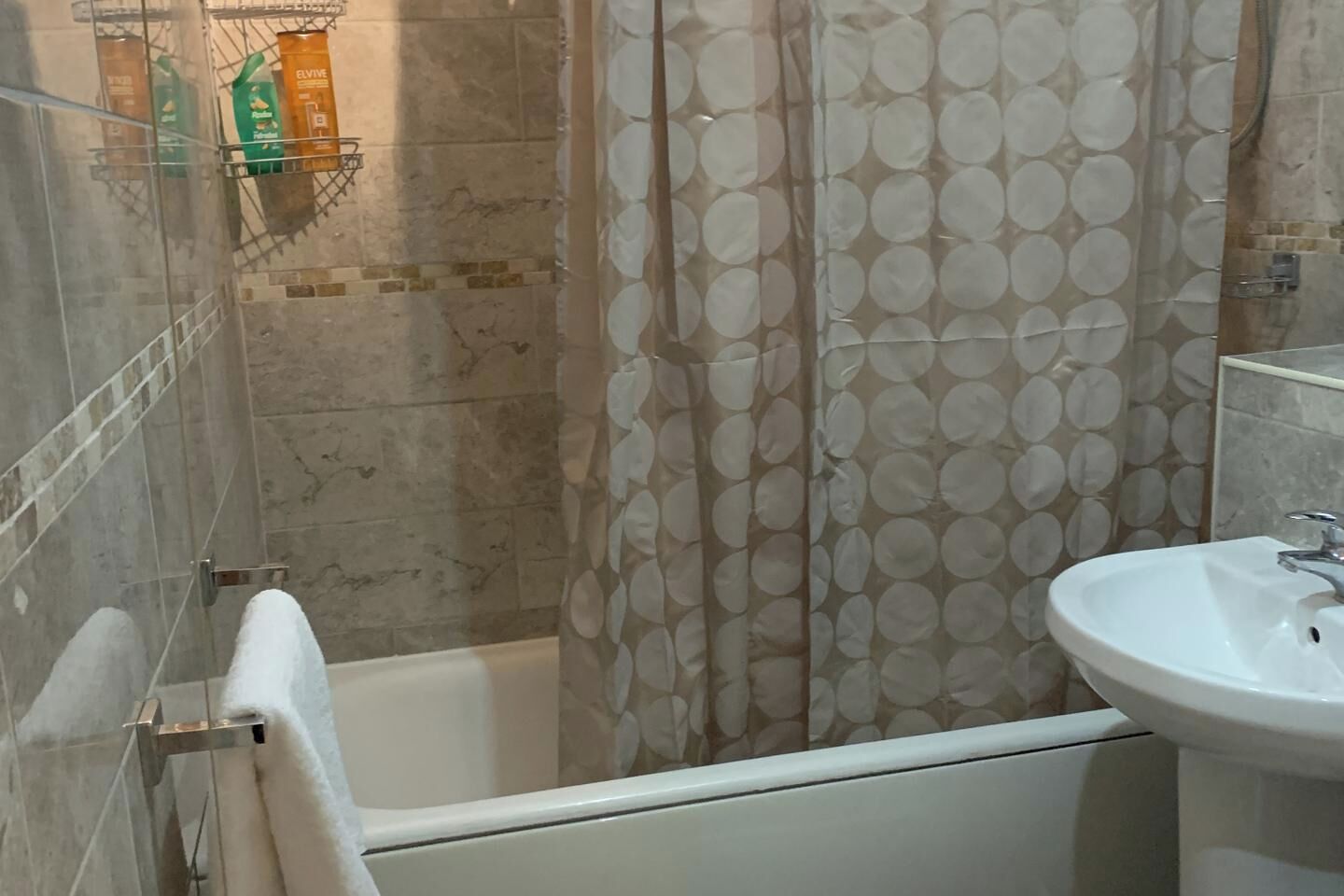 Een badkamer met een bad, een douchegordijn met een rond patroon en een wastafel.