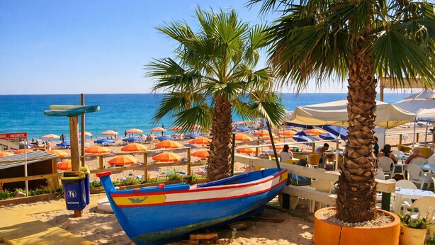 A beachside restaurant with outdoor seating, palm trees, and a blue boat. - T3  Familiar Albufeira, wifi, a/c, praia a 500m (Albufeira)