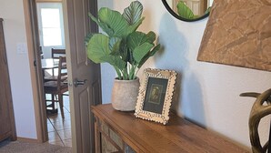 Et trækonsolbord med en potteplante og et indrammet billede. Et spejl hænger på væggen over bordet.