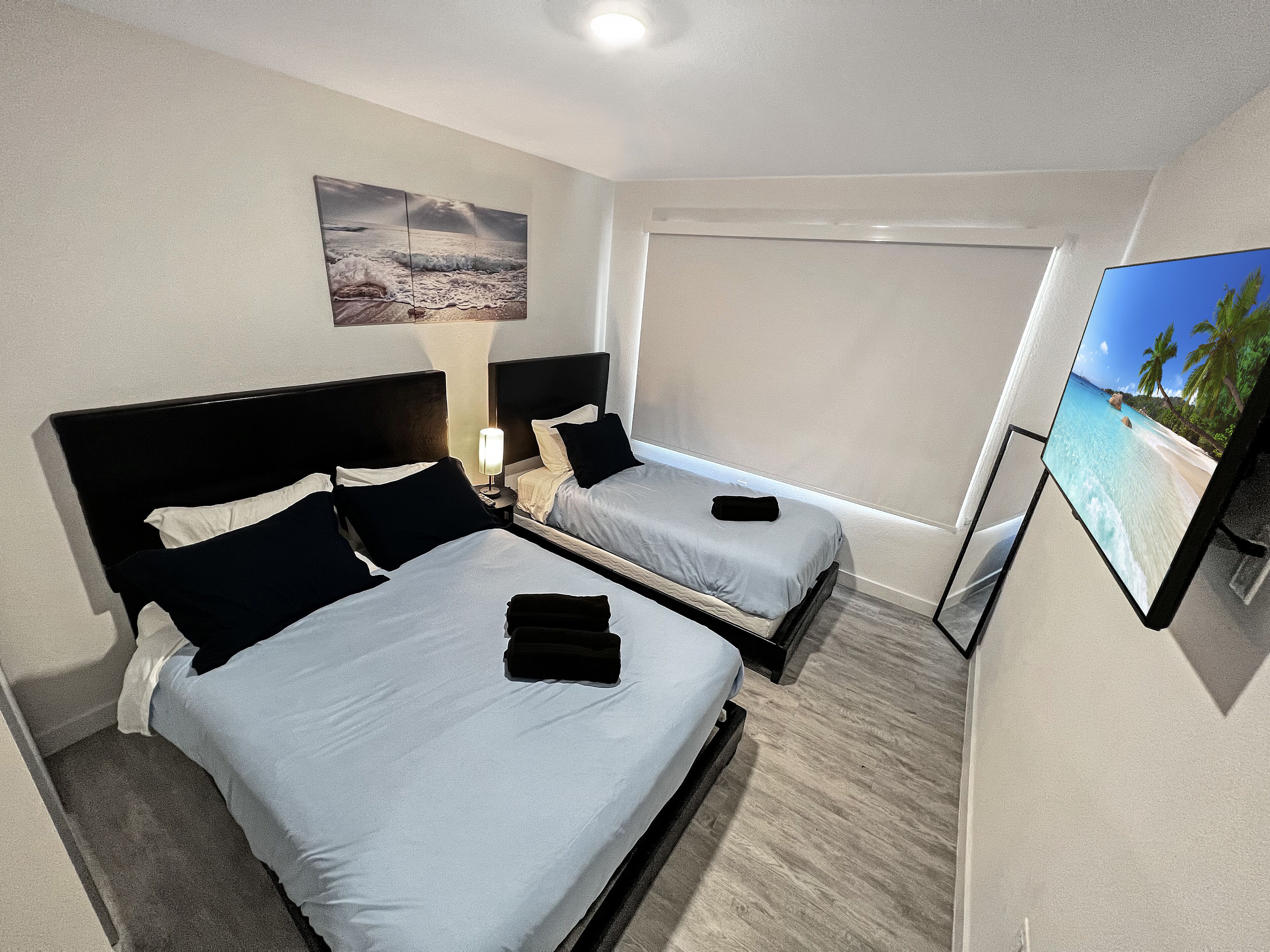 Une chambre d’hôtel avec deux lits, un tableau au mur et un téléviseur diffusant une scène de plage.
