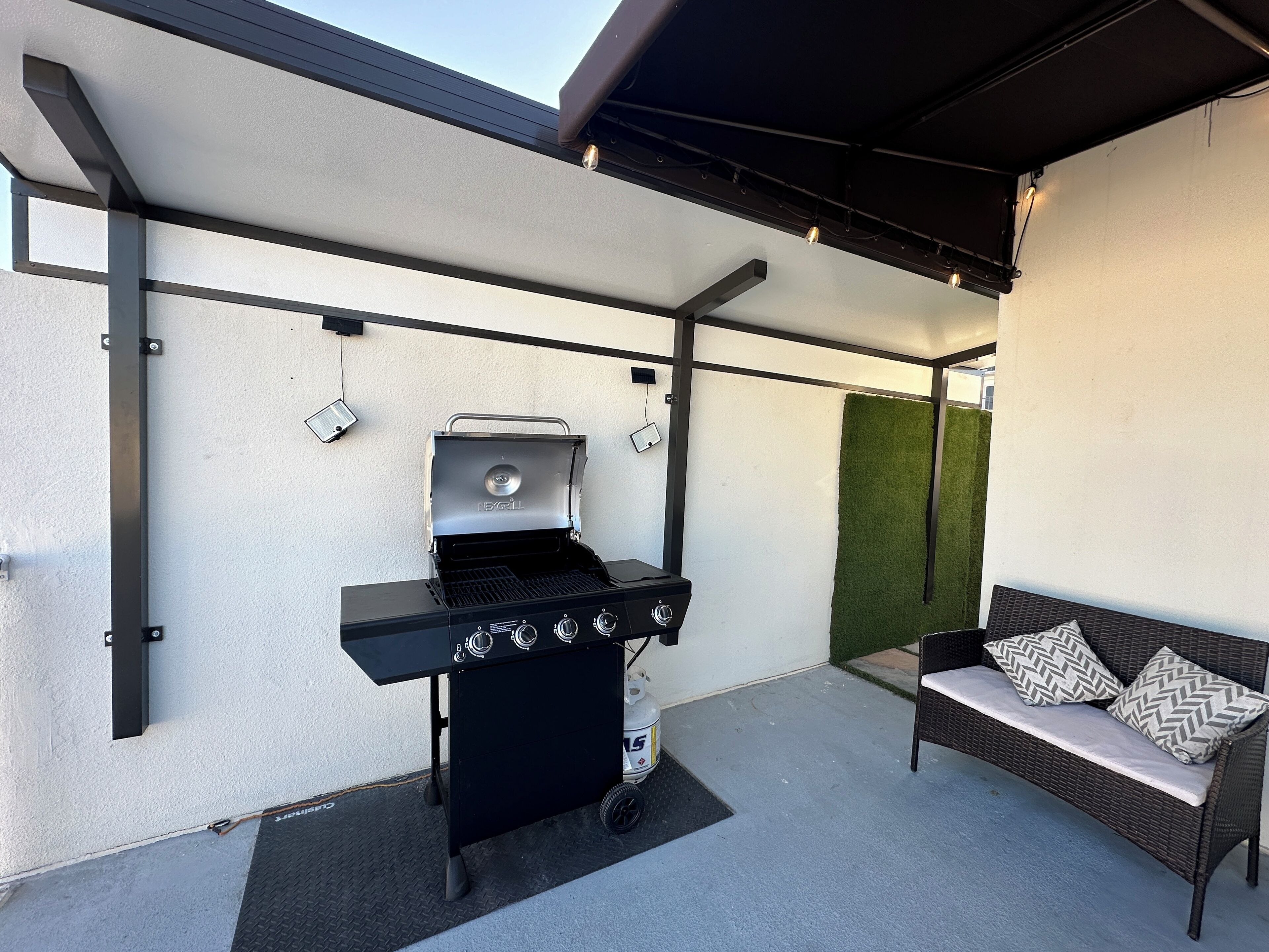Une terrasse avec un barbecue noir, un canapé en osier agrémenté de coussins à motifs et un mur végétal.