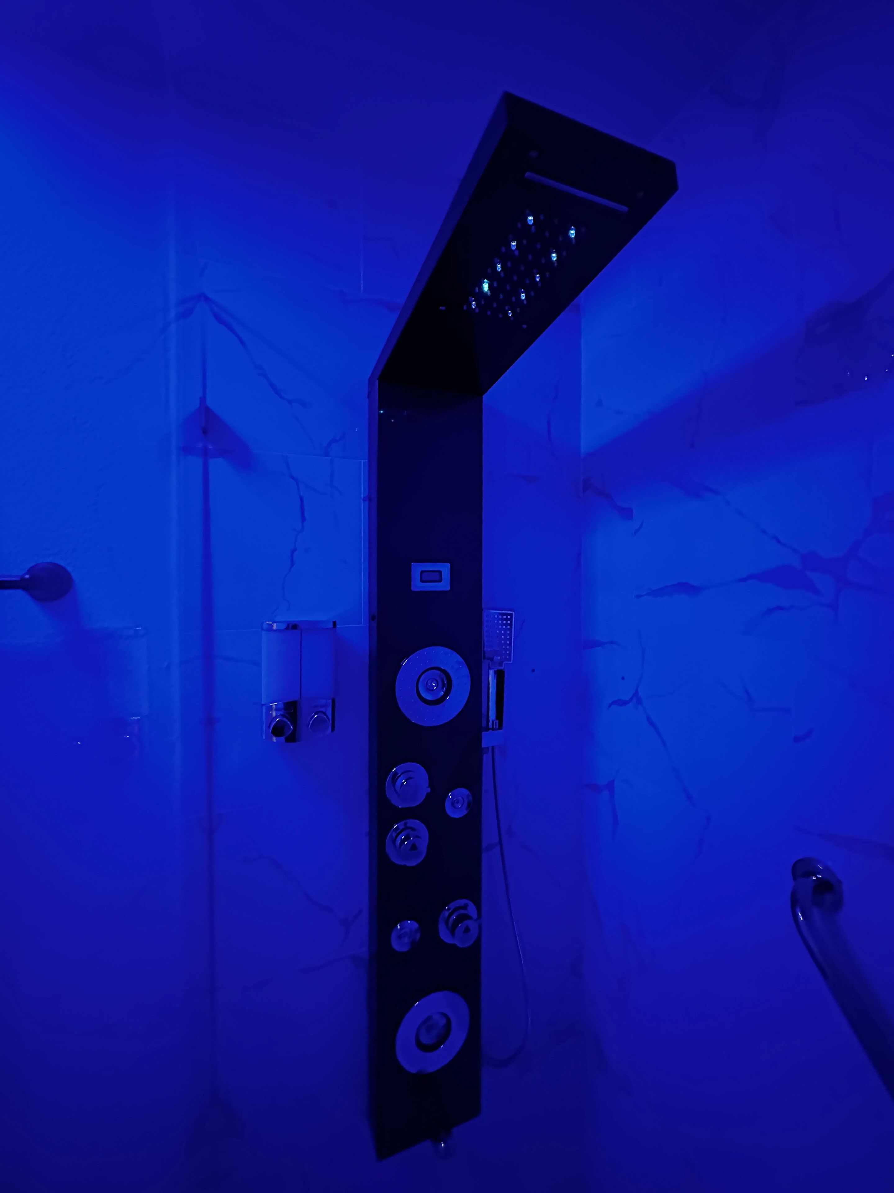 A modern bathroom with a black, wall-mounted shower control panel featuring multiple buttons and a digital display.