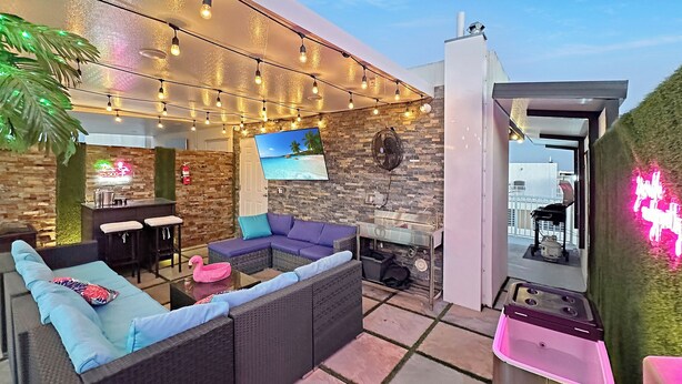 Eine moderne Lounge im Freien mit einer Couch, Barhocker, einer Flamingo-Dekoration und Lichterketten.