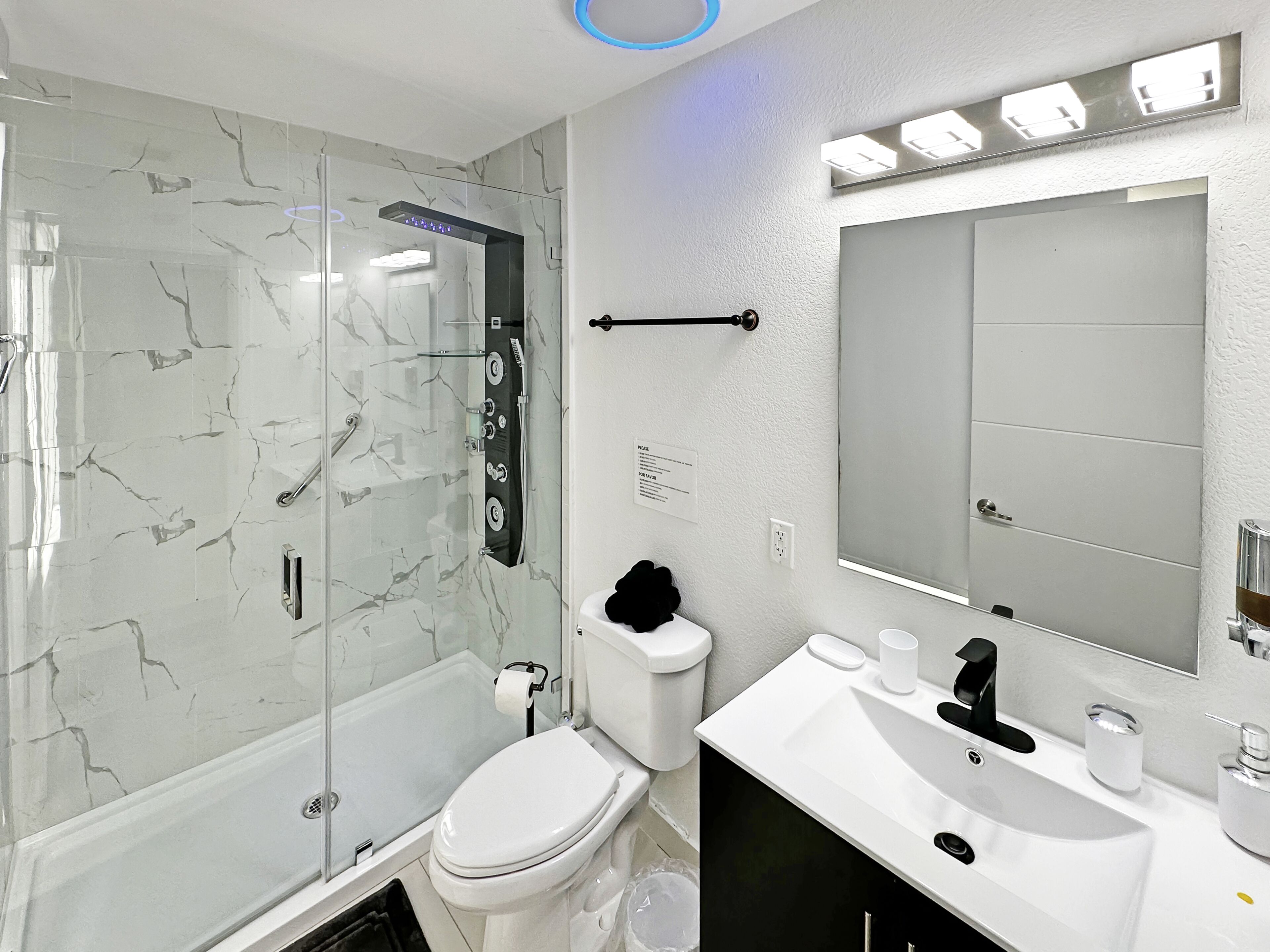 A modern bathroom with a glass-enclosed shower, a toilet, and a sink with a mirror.