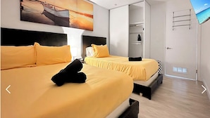 Ein Hotelzimmer mit zwei Betten, jeweils mit gelber Bettwäsche und schwarzen Kopfteilen. Darüber an der Wand hängt ein großes Gemälde, und eine Schiebetür führt ins Badezimmer.