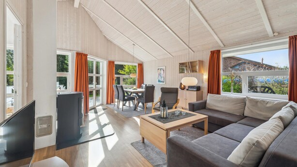 A spacious living area with a large sofa, a coffee table, and a dining table. There are multiple windows providing natural light and views of the outdoors. - Cozy home in Otterndorf with sauna (Otterndorf)