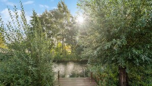 A wooden pathway leading to a body of water, surrounded by dense greenery and trees. - Cozy home in Otterndorf with sauna (Otterndorf)