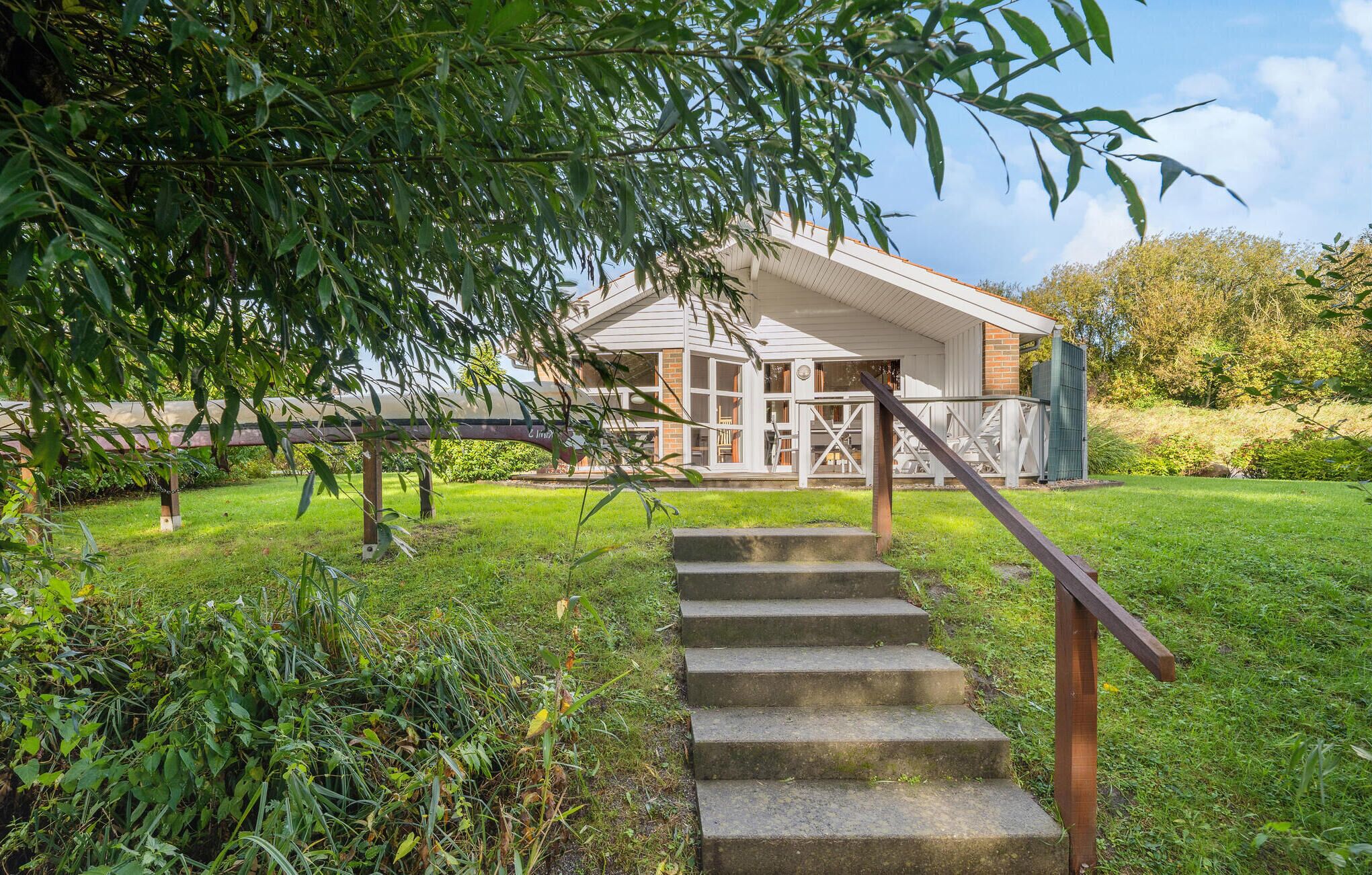A house with a staircase leading to a porch, surrounded by lush greenery and trees.