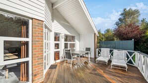 A covered outdoor deck with a dining table and chairs, a wooden floor, and a view of a garden with trees and a fence. - Cozy home in Otterndorf with sauna (Otterndorf)