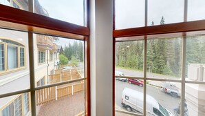 A view from a window overlooking a street with parked cars and a forested area. - Hearthstone Lodge #321 (Sun Peaks)
