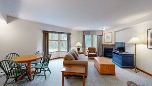A living room with a sofa, chairs, a table, a television, and a fireplace. - Hearthstone Lodge #321 (Sun Peaks)