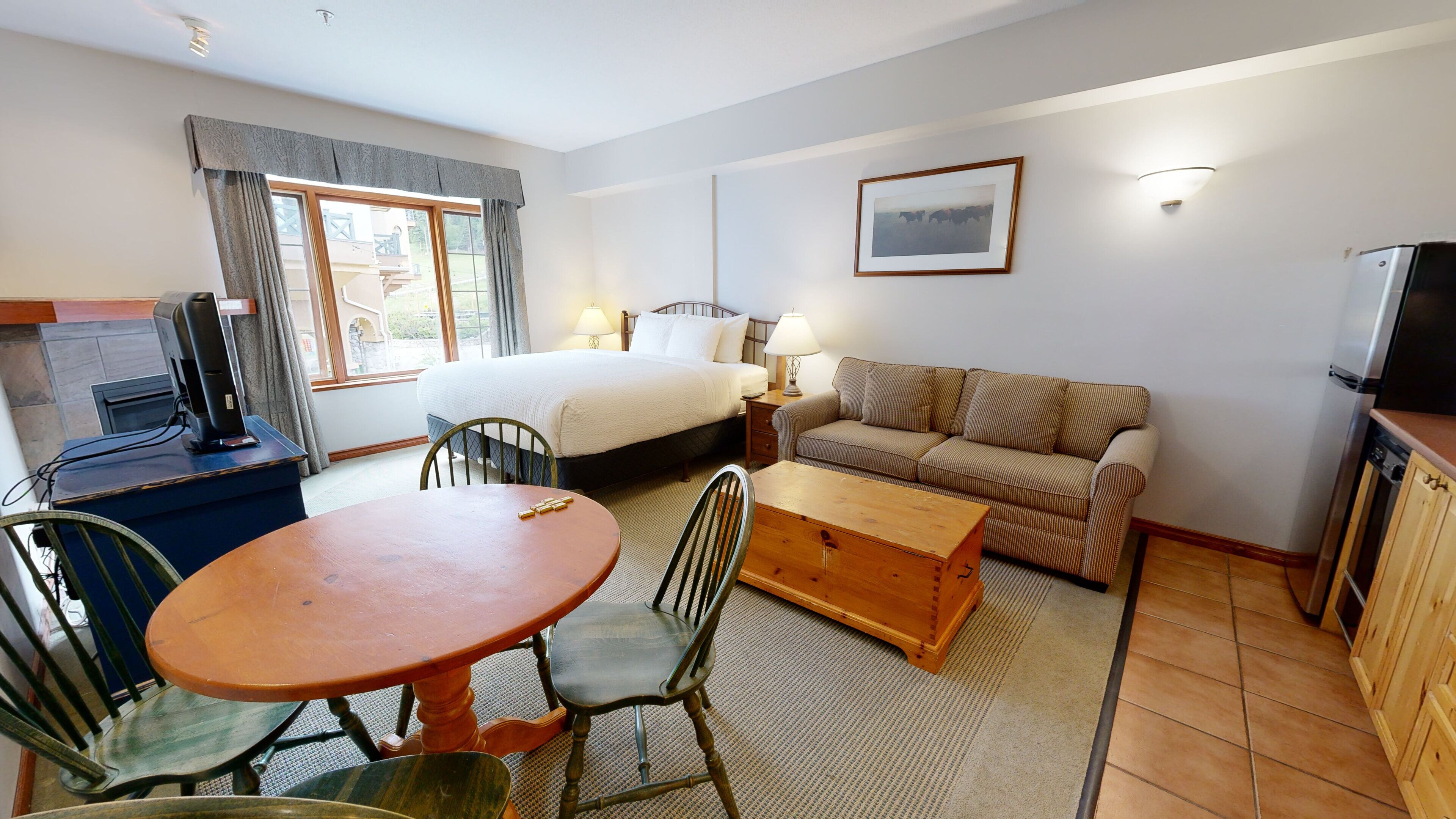 A hotel room with a bed, a sofa, a dining table with chairs, a TV, and a window with curtains.