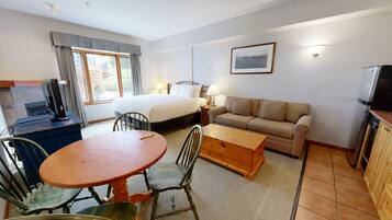 A hotel room with a bed, a sofa, a dining table with chairs, a TV, and a window with curtains.