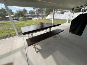 A picnic table with a bowl on top, located in an outdoor covered area with a view of a grassy field and a body of water.