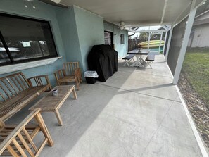 A covered patio area with wooden benches, a table, and a grill.