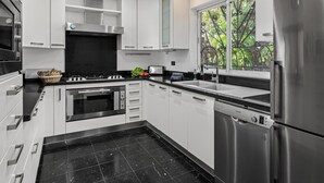 Een moderne keuken met witte kasten, een roestvrijstalen koelkast, een vaatwasser en een raam met uitzicht op groen.