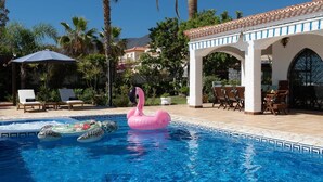 Zwembad met opblaasbare flamingo's en vissen, omringd door palmbomen en een overdekt terras.