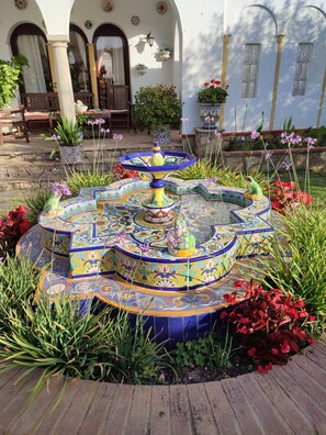 Ein farbenfroher Brunnen mit aufwendiger Kachelkunst, umgeben von verschiedenen Pflanzen und Blumen.
