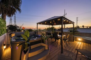 En takterrass med ett bubbelbad, utomhusmöbler och en pergola dekorerad med ljusslingor.