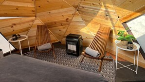 A cozy, triangular wooden tent with a fireplace, two chairs, a small table, and a potted plant. - Raptor Ranch (Williams)