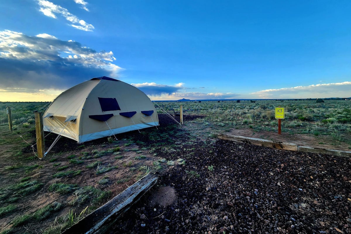 A dome-shaped tent with a flat roof, surrounded by a fenced area with a dirt path leading to it.