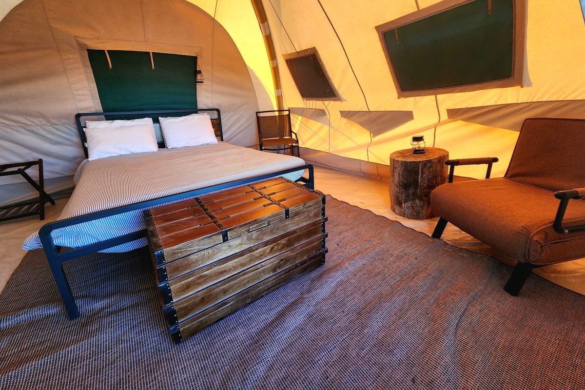 A tented room with a bed, a chair, a small table, and a window.