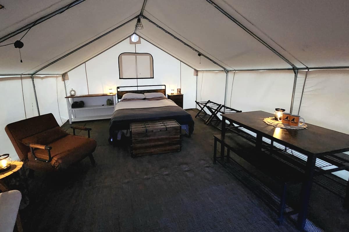 A tented accommodation with a bed, a table, and chairs.