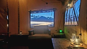 A cozy room with a view of a snowy landscape through a large window, a comfortable chair, a small table with a lantern, and a wall-mounted lamp. - Raptor Ranch (Williams)