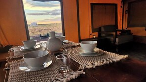 A dining table set with bowls and glasses, a vase, and a view of a desert landscape through a window. - Raptor Ranch (Williams)